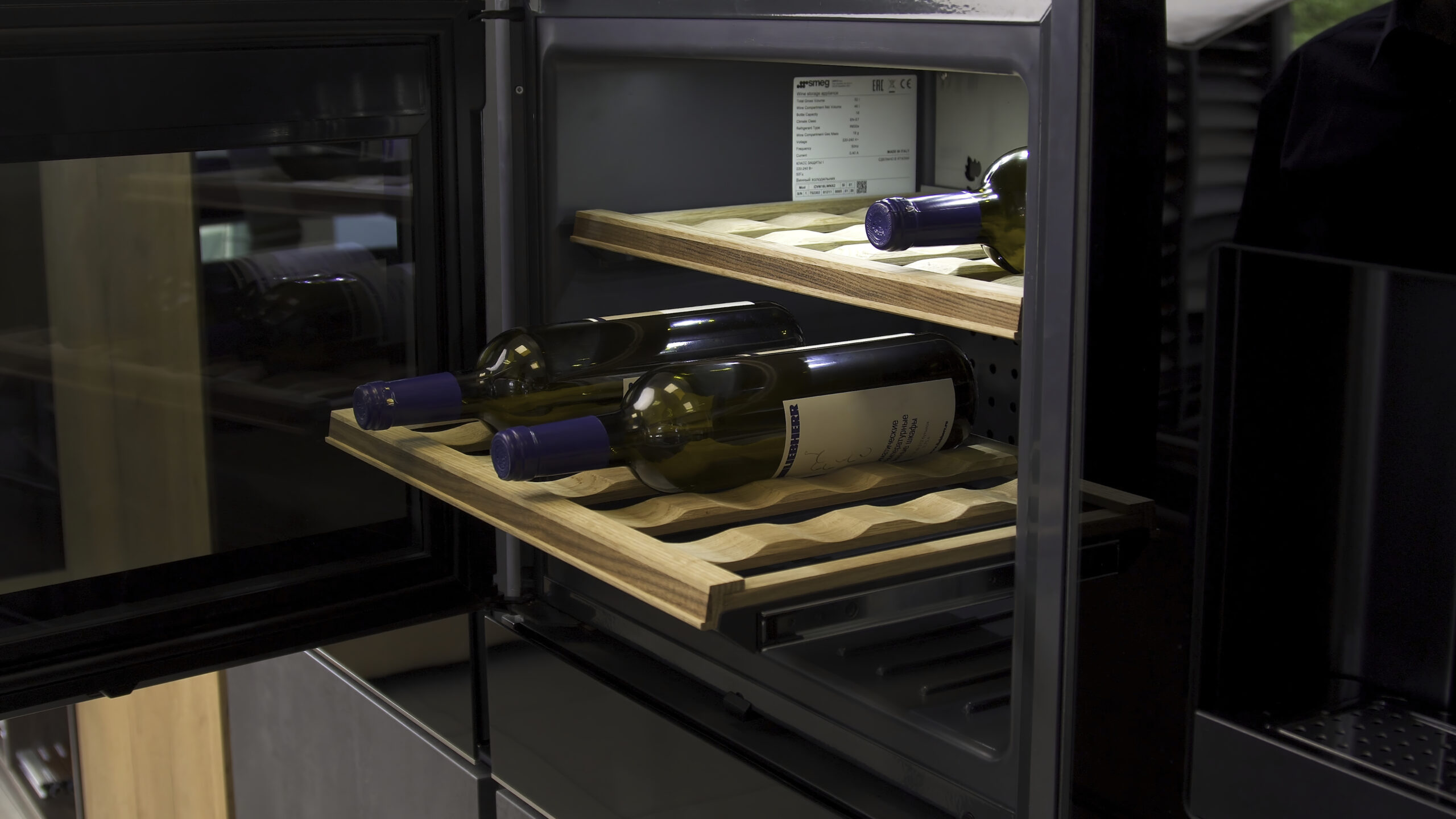 Wine bottles cooling on refrigerator wooden shelves. Household utensils. Close up of home use wine cooler, man closes the door of a cooling machine.